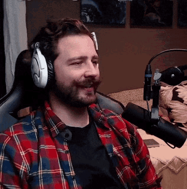a man wearing headphones and a plaid shirt is sitting in front of a microphone in a chair .