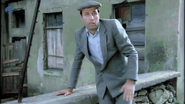 a man in a suit and hat is leaning against a wall