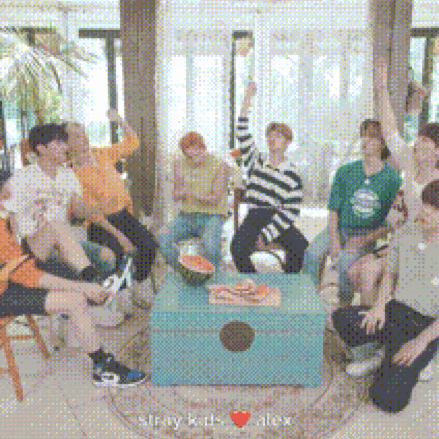 a group of young people are sitting around a table with watermelons on it .