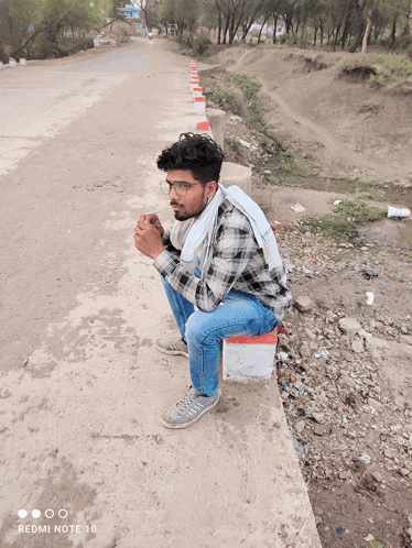 a man squatting on the side of a road with a redmi note 10 in the background