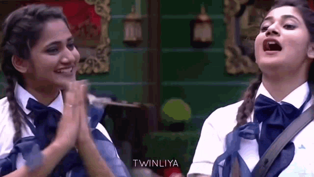two girls wearing school uniforms and bow ties are clapping their hands in a room .