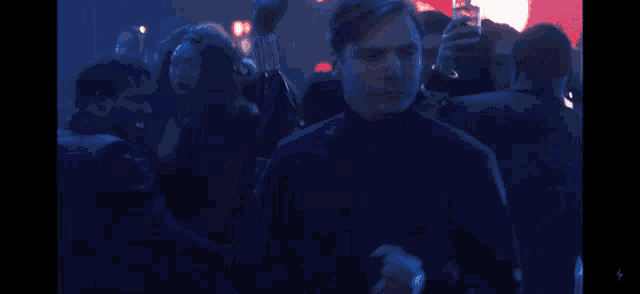 a man in a blue jacket stands in a crowd of people .