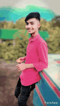 a young man wearing a pink shirt is leaning against a wall and smiling