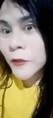 a close up of a woman 's face wearing a yellow shirt and making a funny face .