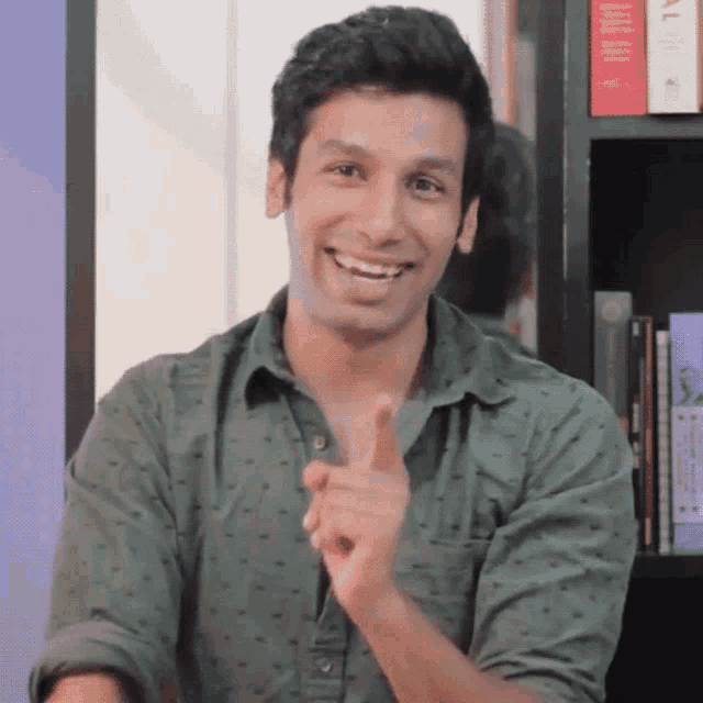a man in a green shirt is smiling and pointing at something