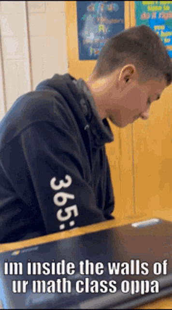 a man wearing a 365 sweatshirt sits at a desk in a math class