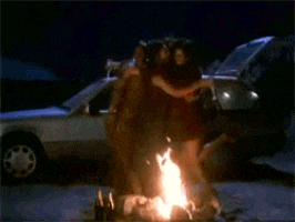 a man and a woman are standing next to a car that is on fire .