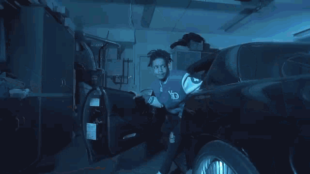 a man is standing next to a black car in a garage with the door open .