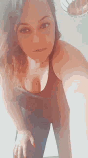 a woman in a black tank top is taking a selfie with her hand on her hip .