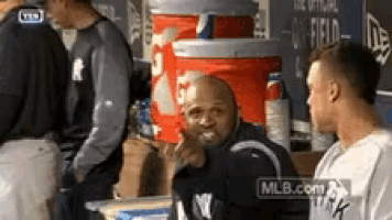 a man in a new york yankees shirt is pointing at something while standing in a dugout .
