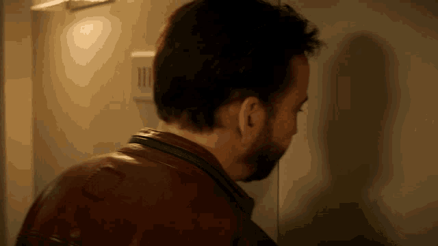 a man wearing a brown leather jacket is standing in front of a door