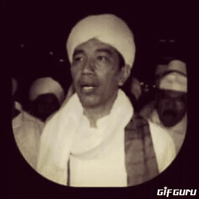a man wearing a turban and a white scarf stands in front of a crowd