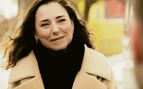 a woman wearing a black turtleneck and a white coat smiles