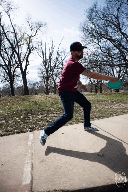 a man in a maroon shirt is throwing a frisbee on the sidewalk