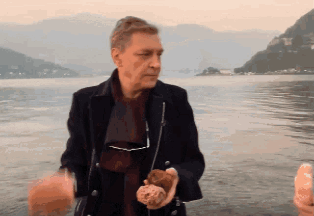 a man standing in front of a body of water holding a piece of bread