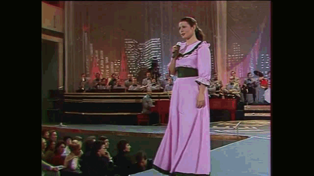 a woman in a pink dress sings into a microphone