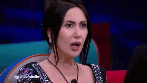 a woman in a black dress is sitting on a red couch with the words grandefratello on the bottom