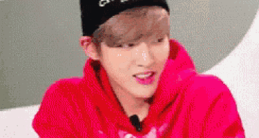 a young man wearing a red hoodie and a black hat is looking at the camera .