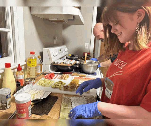 a woman wearing a red shirt that says sushi club is preparing food in a kitchen