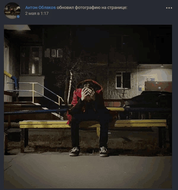 a man in a red jacket sits on a bench with his hands on his face