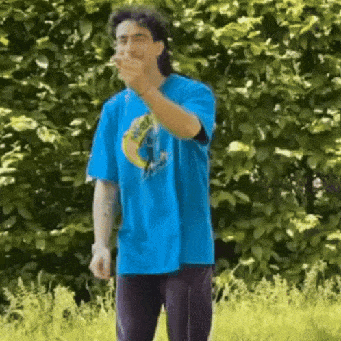 a man in a blue shirt is standing in the grass and pointing at the camera .