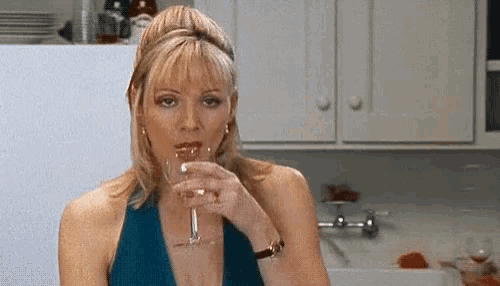 a woman in a blue dress is holding a glass of wine in a kitchen .