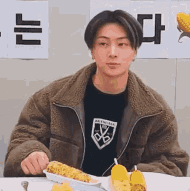 a young man is eating corn on the cob at a table .