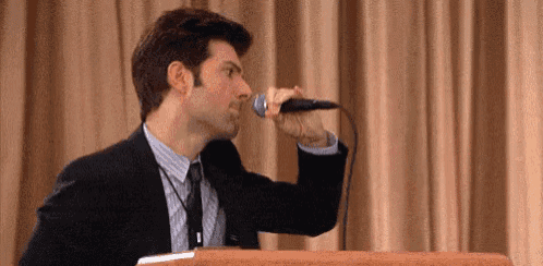 a man in a suit and tie is singing into a microphone while standing behind a podium .