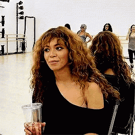 a woman with curly hair is sitting in a chair and holding a drink