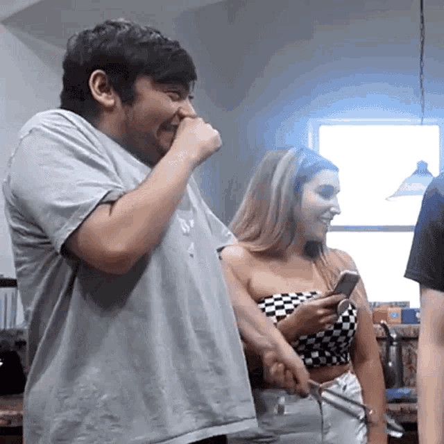 a man and a woman are standing in a kitchen . the woman is holding a cell phone .