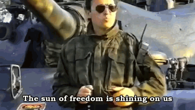 a man in a military uniform is standing in front of a tank with the words the sun of freedom is shining on us .
