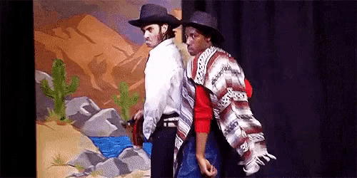 two men are standing back to back on a stage in front of a painting .