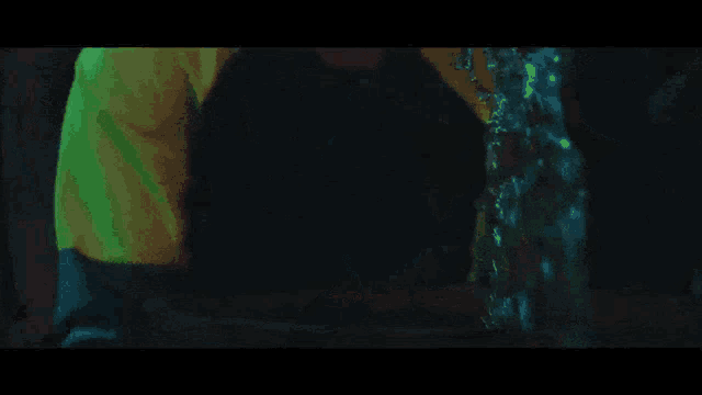 a man wearing a neon green shirt is dancing in a dark room