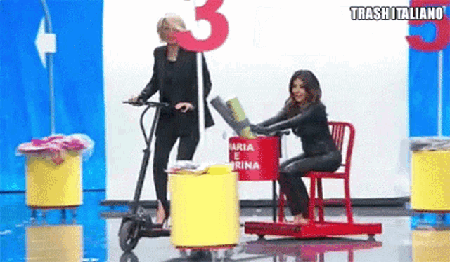 a woman is sitting in a chair while another woman is riding a scooter .