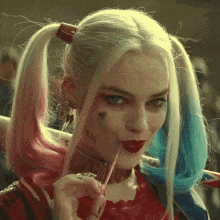 a woman in a harley quinn costume is holding a bat and a cigarette in her mouth .
