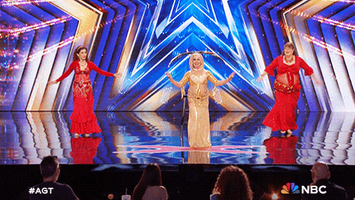 a group of belly dancers are performing on a stage in front of a crowd of people .