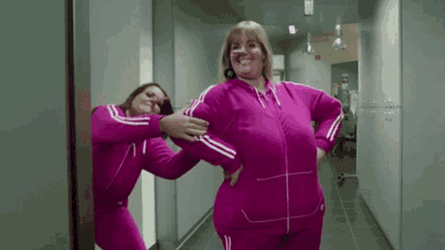 a woman in a pink tracksuit is standing next to another woman in a pink tracksuit in a hallway .