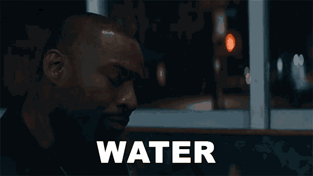 a man is sitting in front of a window and the word water is on the screen behind him