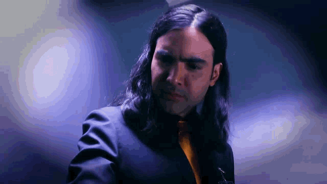 a man with long hair is wearing a suit and a yellow tie