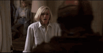a woman in a white shirt is standing in front of a jason voorhees holding a bat