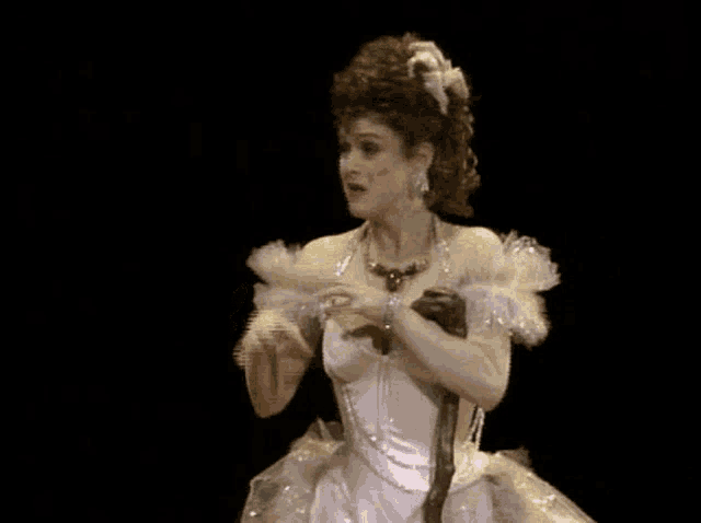 a woman in a white dress is holding a cane on a stage in front of a black background .