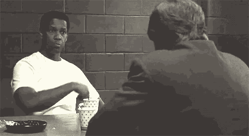 two men are sitting at a table talking to each other in a room .