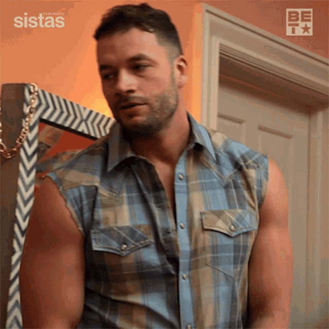 a man in a plaid shirt is standing in front of a door with the words sistas written on the wall behind him