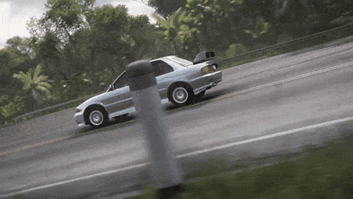 a silver car is driving down a road with trees in the background .