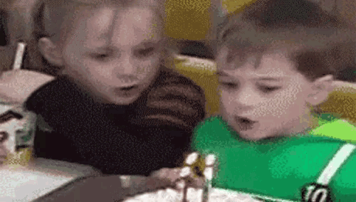 a boy and a girl are sitting at a table looking at a cake .