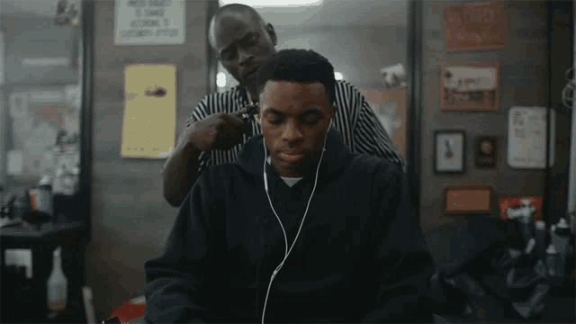 a man wearing headphones is getting his hair cut by a man wearing a striped shirt