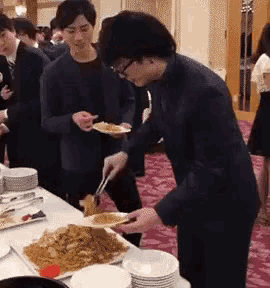 a group of people standing around a table with plates of food on it .