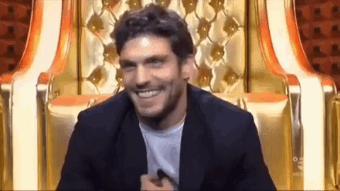a man in a suit is smiling while sitting on a chair .