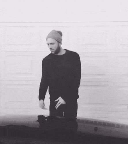 a man wearing a beanie and a black sweater is kneeling down in front of a garage door