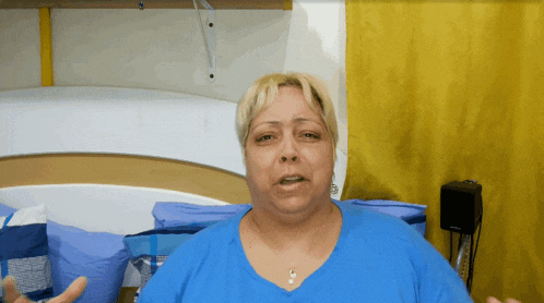a woman in a blue shirt is sitting in front of a bed with pillows